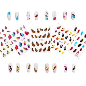 May include: Nail art stickers featuring colorful feather designs. The image shows several sheets of nail decals with various feather patterns in shades of blue, red, yellow, and brown. Some nails are also decorated with feather designs.