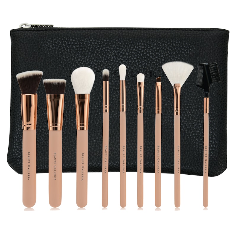 Op de afbeelding: Een set van negen make-upkwasten met ros&eacute;gouden handvatten en witte haren. De kwasten zijn gerangschikt in een zwarte ritszak met de merknaam "BEAUTE GALLERIA" gedrukt op elk handvat.