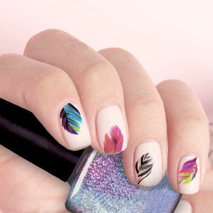 May include: A hand with painted nails featuring colorful feather designs. The nails are painted white with feather art in shades of blue, purple, pink, and green. A bottle of nail polish is in the background.