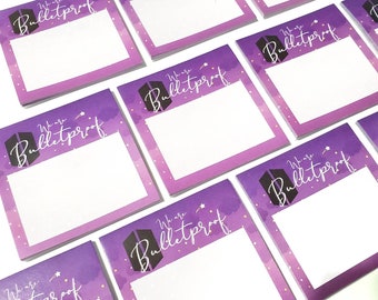 May include: A stack of purple and white notepad paper with the text "We are Bulletproof" printed on each sheet. The paper has a watercolour background with gold stars.