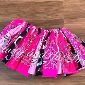May include: A pink and black bandana skirt with a white paisley pattern. The skirt is made of multiple bandanas sewn together and has a gathered elastic waistband.
