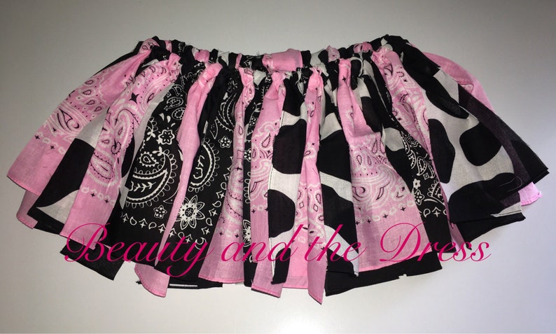 May include: A pink and black tutu skirt with a cow print and paisley pattern. The skirt is made of fabric scraps and has a gathered elastic waistband.