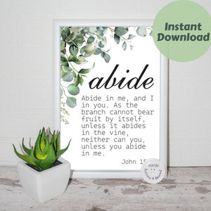 May include: A white framed print with a watercolor illustration of eucalyptus leaves. The print features the word "abide" in large, bold letters and a quote from John 15:4 in black text. The quote reads: "Abide in me, and I in you. As the branch cannot bear fruit by itself, unless it abides in the vine, neither can you, unless you abide in me."