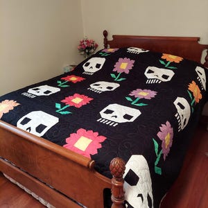 May include: A black quilt with a white skull and flower pattern. The quilt is on a wooden bed frame with a wooden headboard.