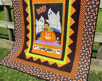 Könnte beinhalten: Ein Halloween-Quilt mit einem zentralen Feld mit zwei weißen Geistern, einem geschnitzten orangefarbenen Kürbis und dem Wort „BOO!“. Der Quilt hat einen schwarzen Rand mit orangefarbenen und grünen Akzenten und einen gemusterten Rand mit Kürbissen und Süßigkeiten.
