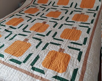 May include: A handmade quilt featuring a repeating pattern of orange pumpkins on a cream background. The pumpkins are framed by green and brown geometric shapes. The quilt is placed on a wooden bed frame, showcasing a cozy, autumnal theme.