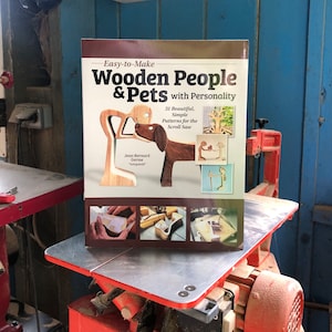 Könnte beinhalten: Ein Buch mit dem Titel "Easy-to-Make Wooden People & Pets with Personality" mit einem Titelbild einer Holzfigur und eines Hundes. Das Buch enthält 31 Muster für Laubsägearbeiten.