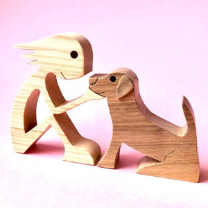 Peut inclure: Une figurine en bois d'une personne avec des cheveux longs et flottants tendant la main vers une figurine de chien en bois. Les deux figurines sont en bois brun clair.