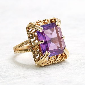 May include: A gold ring with a large, faceted, purple amethyst gemstone set in a delicate, filigree design.