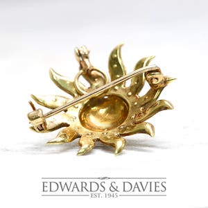 May include: A gold sunburst brooch with a round center and a pin on the back. The brooch is made of 14k gold and is set with diamonds.