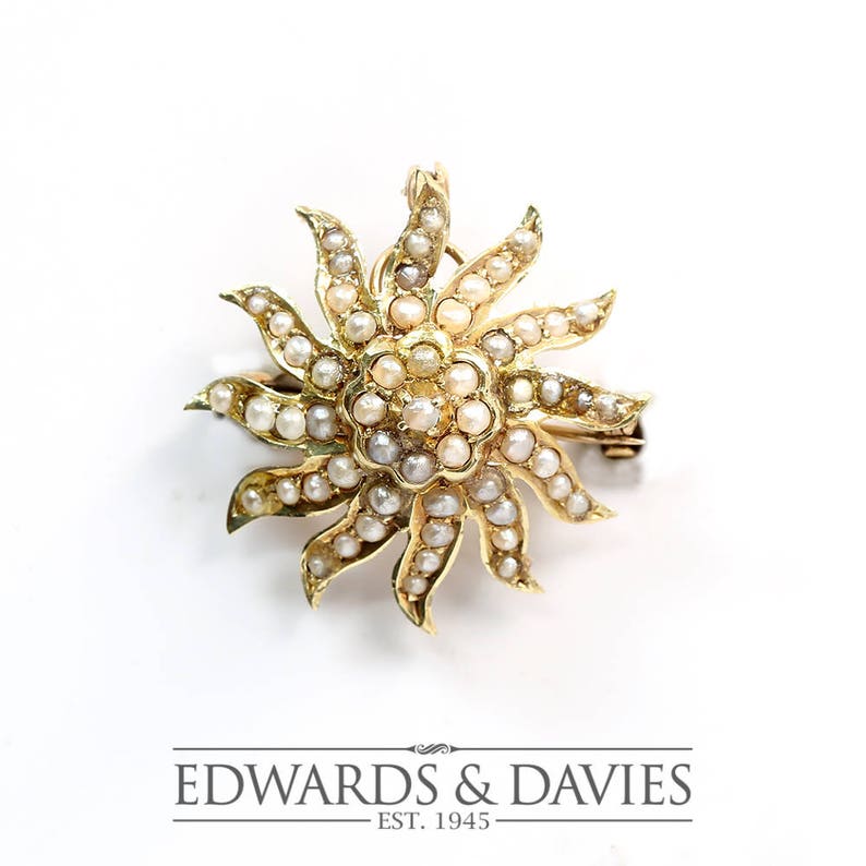 May include: A gold brooch in the shape of a sun with a center of small pearls and rays of larger pearls.