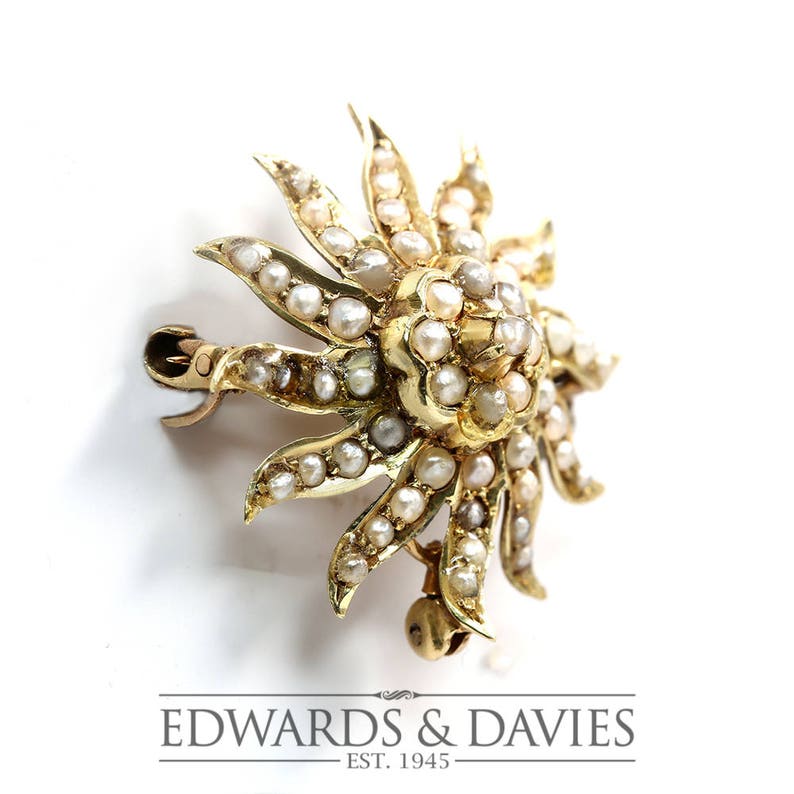 May include: A gold sunburst brooch with a center of pearls and a pearl-set border. The brooch has a pin and catch closure.