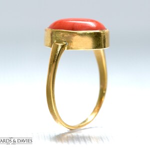 May include: A gold ring with a red coral gemstone. The ring is set in a simple, oval-shaped setting.
