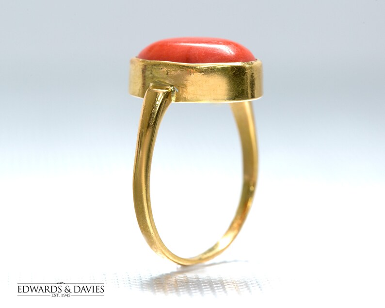 May include: A gold ring with a red coral gemstone. The ring is set in a simple, oval-shaped setting.