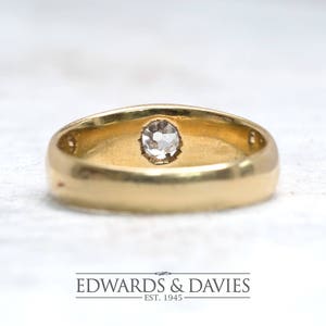 Pode incluir: Um anel de banda de ouro com uma &uacute;nica gema oval transparente engastada no centro.