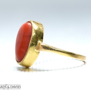 May include: A gold ring with a large, oval-shaped, red coral gemstone.