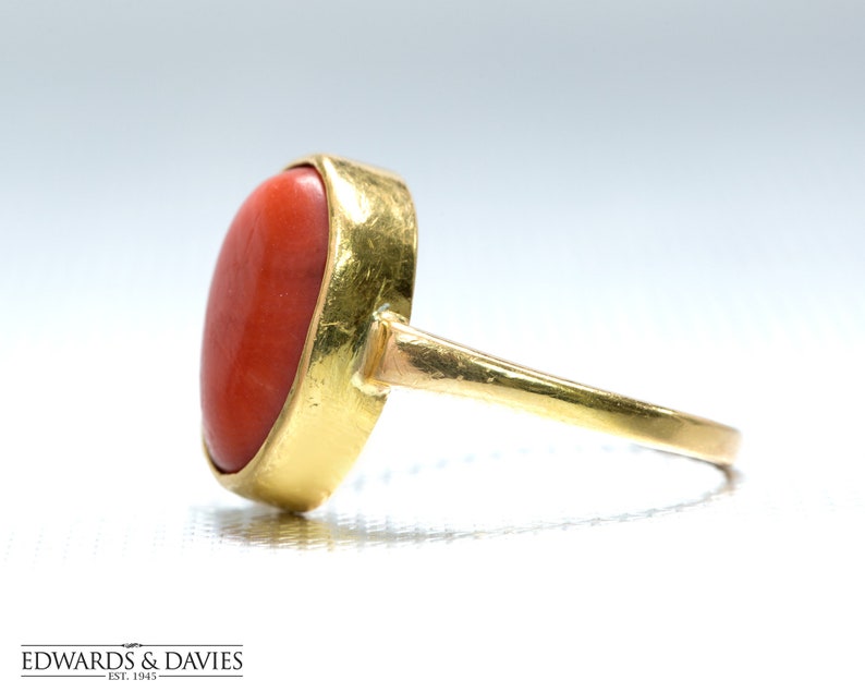 May include: A gold ring with a large, oval-shaped, red coral gemstone.