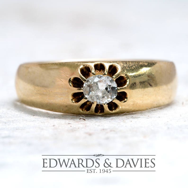 Pode incluir: Um anel de banda de ouro com um &uacute;nico diamante redondo engastado em um design em forma de flor. O anel &eacute; de estilo cl&aacute;ssico.