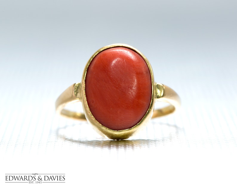 May include: A gold ring with a large oval-shaped red coral gemstone.