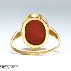 May include: A gold ring with a red oval-shaped gemstone. The ring is viewed from the back, showing the setting of the stone.