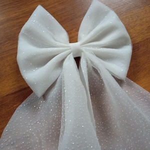 May include: A white tulle bow with a sparkly finish. The bow is tied with a loop and has long tails.