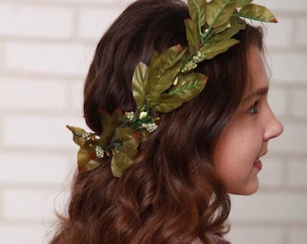 May include: A girl with long brown wavy hair wearing a leafy green floral crown.