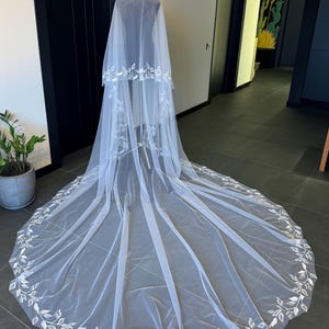 May include: A white bridal veil with a delicate floral design. The veil is made of soft tulle and features a scalloped edge. The veil is long and flowing, and it would be perfect for a wedding ceremony or reception.