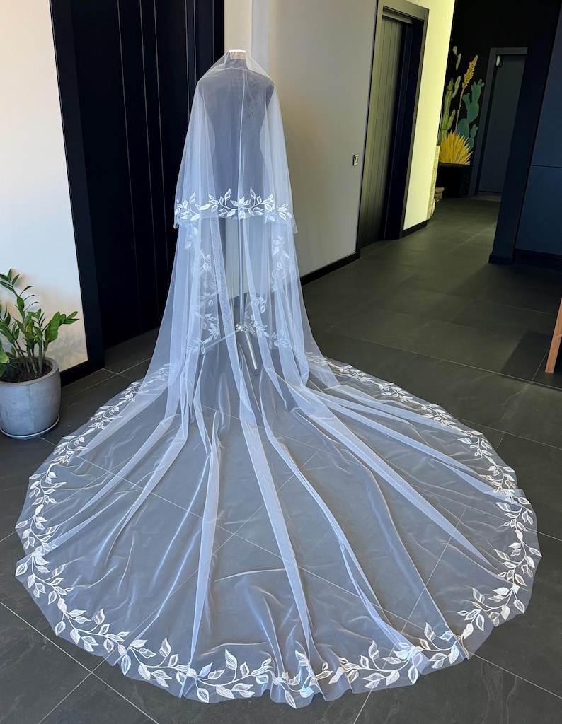 May include: A white bridal veil with a delicate floral design. The veil is made of soft tulle and features a scalloped edge. The veil is long and flowing, and it would be perfect for a wedding ceremony or reception.