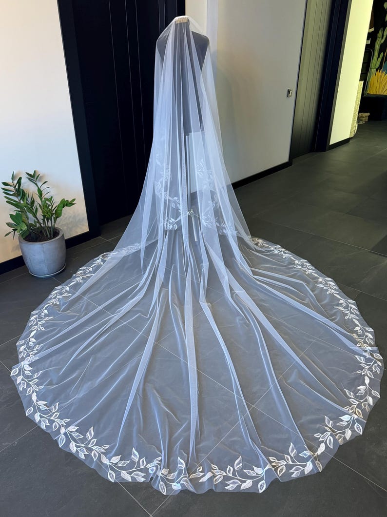 May include: A white tulle wedding veil with a delicate floral embroidery design around the edge.
