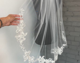 May include: A white bridal veil with a delicate lace trim. The veil is made of soft tulle and has a single layer.