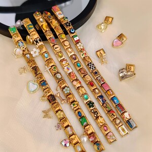 May include: Gold charm bracelets with a variety of colourful charms, including hearts, flowers, and flags. Several bracelets are displayed, along with individual charms. The charms feature enamel and crystal accents.