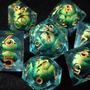 Puede incluir: Un conjunto de dados poliédricos con una combinación de colores turquesa y verde. Los dados tienen números dorados y un diseño verde y amarillo en el interior. Los dados están hechos de un material transparente y claro.