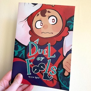 May include: A comic book cover with a red, white, and black jester character. The title is "A Duel of Fools" with a green background and a green jester hat icon. The author is "Cat Laird".
