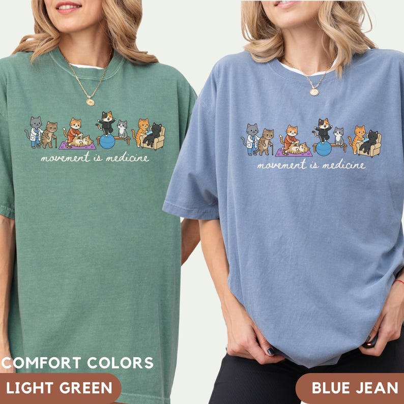 May include: A light green and a blue jean t-shirt, each featuring a graphic illustration of various cats performing physical therapy exercises with the text "movement is medicine" printed in white cursive script below the cat characters.