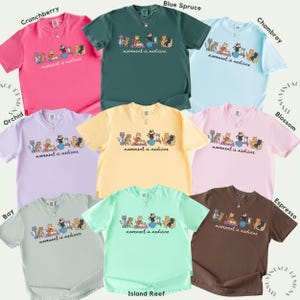 May include: A collection of eight short-sleeve t-shirts in various colors including pink, dark green, light blue, lavender, yellow, light pink, light gray, mint green, and brown. Each shirt features a graphic of cats exercising with the text movement is medicine.