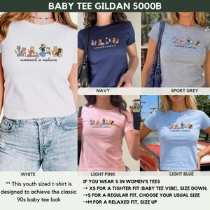 May include: A collection of Gildan 5000B baby t-shirts in white, navy, sport grey, light pink, and light blue. Each shirt features a graphic of various cats exercising with the text "movement is medicine" printed in black on the center chest area.