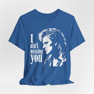 May include: A royal blue short-sleeve t-shirt featuring a white graphic print of a person with long hair in profile. The text "I ain't missing you" is printed in white to the left of the portrait. The shirt has a crew neckline and hem.