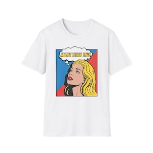 May include: White t-shirt featuring a pop art style graphic. The graphic shows a blonde woman looking up with the text "MORE THAN THIS" in a thought bubble. The background is red and blue.