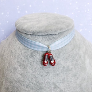May include: A blue and white gingham ribbon choker necklace with a red ruby slipper charm.