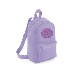 May include: A lavender backpack with a front pocket and a top handle. The backpack features a sparkly purple seashell design on the front. It has adjustable shoulder straps and a zippered main compartment.