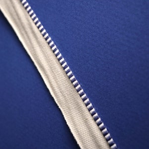 May include: A close-up of a white fabric with blue and white stripes. The fabric is against a solid blue background.