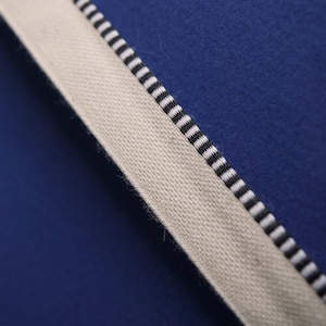 May include: A close-up of a white fabric with black stripes against a blue background. The fabric has a textured surface.