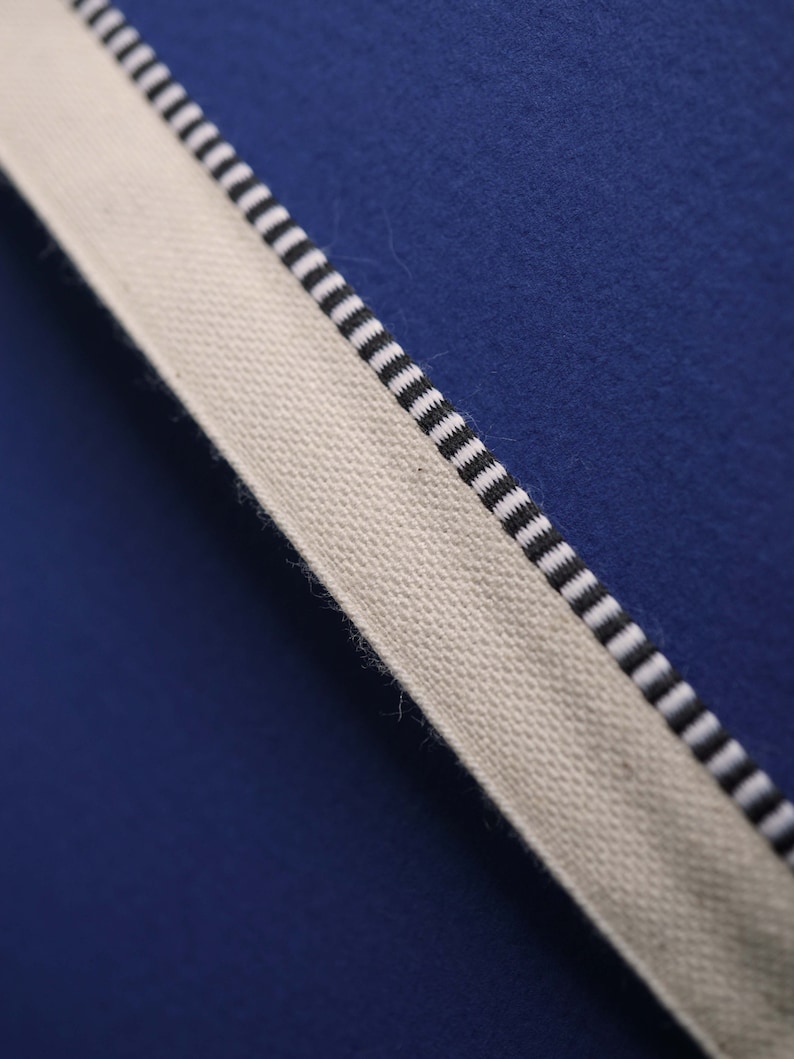 May include: A close-up of a white fabric with black stripes against a blue background. The fabric has a textured surface.