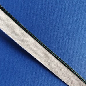 May include: A white fabric ribbon with a black and green striped trim on a blue background.