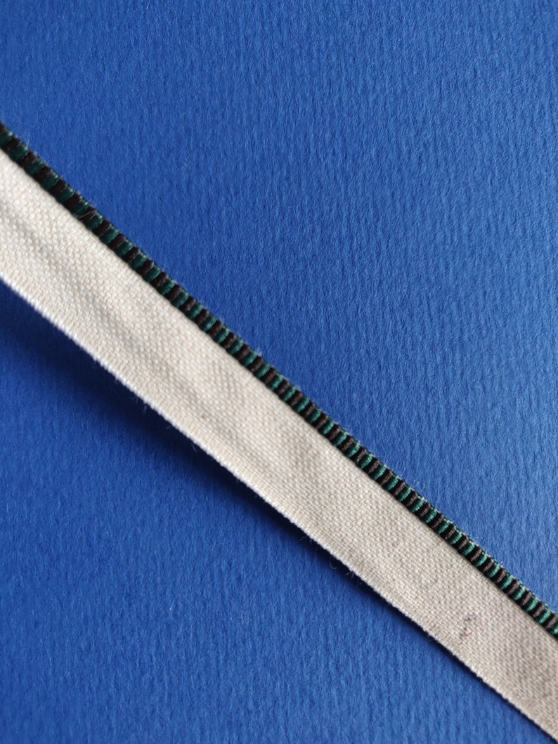 May include: A white fabric ribbon with a black and green striped trim on a blue background.