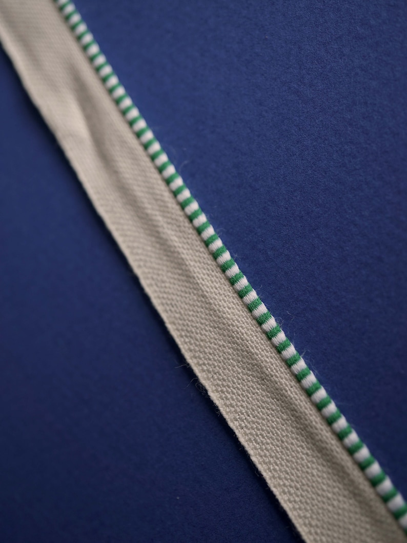 May include: A close-up of a beige fabric with green and white stripes. The fabric is against a dark blue background.