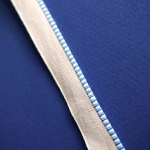 May include: A close-up of a white fabric ribbon with blue stripes against a blue background.