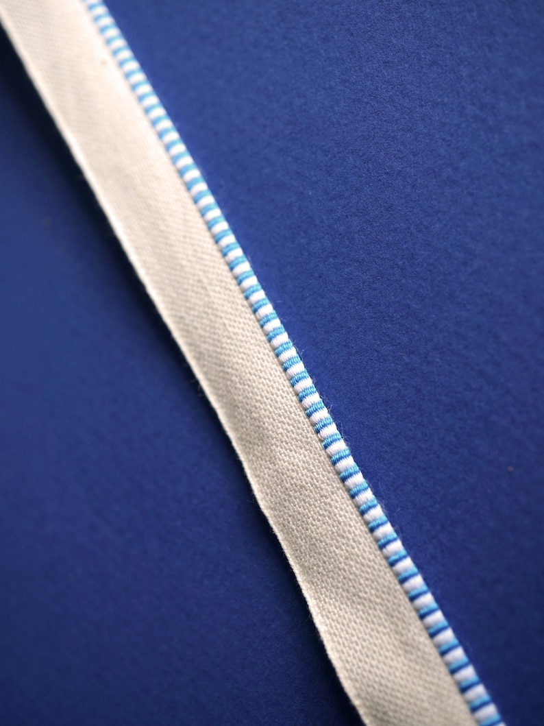 May include: A close-up of a white fabric ribbon with blue stripes against a blue background.