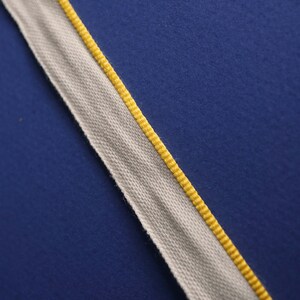 May include: A white fabric ribbon with a yellow edge. The ribbon is on a blue background.