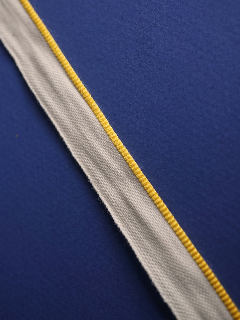 May include: A white fabric ribbon with a yellow edge. The ribbon is on a blue background.